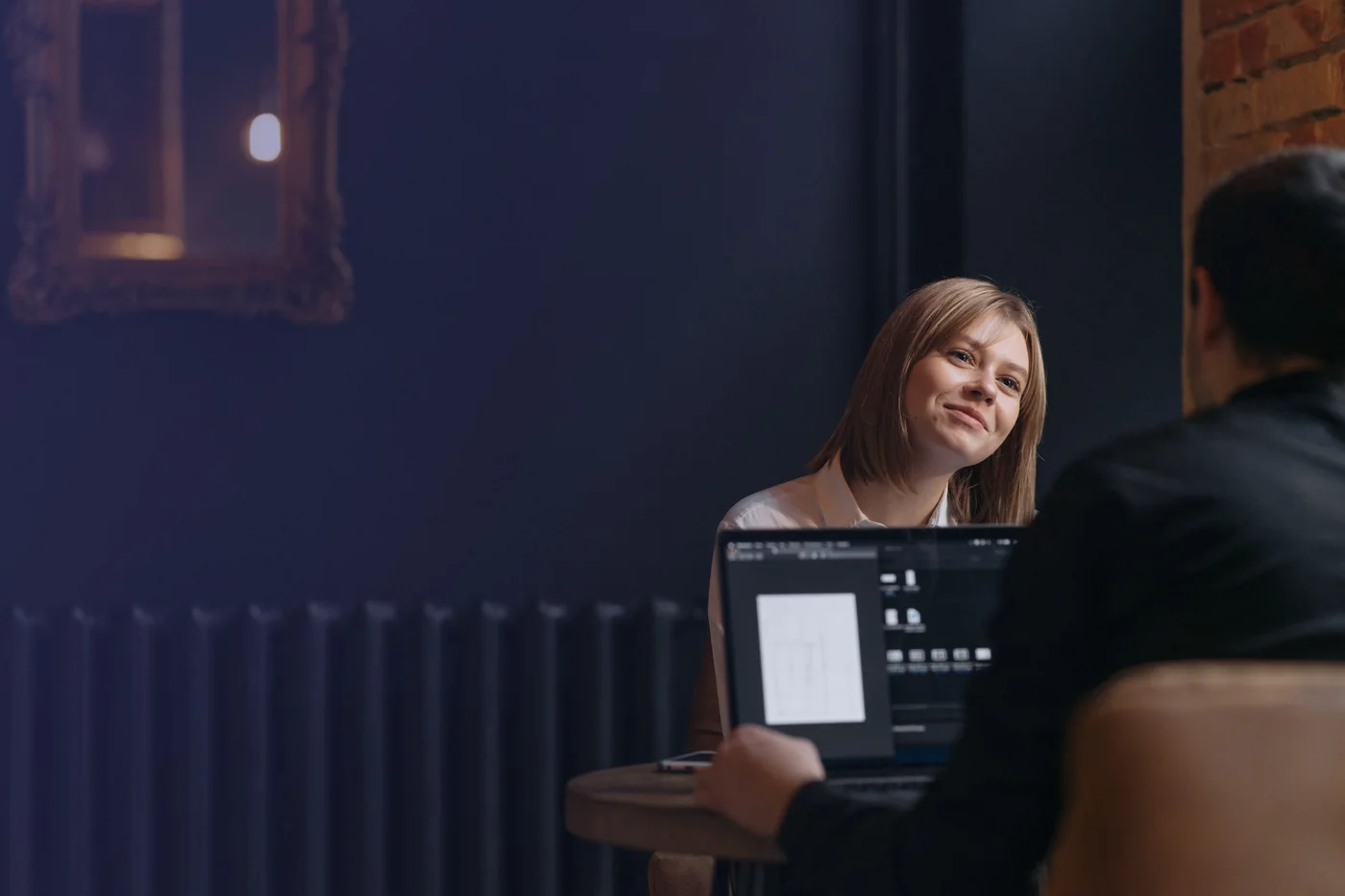 Two people in conversation across a laptop in a dimly lit café