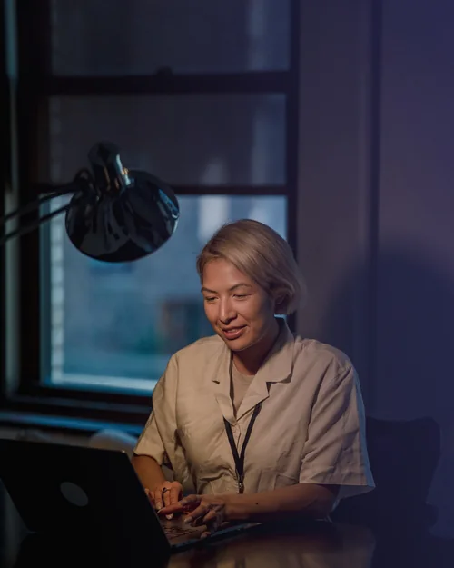 A member of staff answering messages at a laptop under a desk lamp